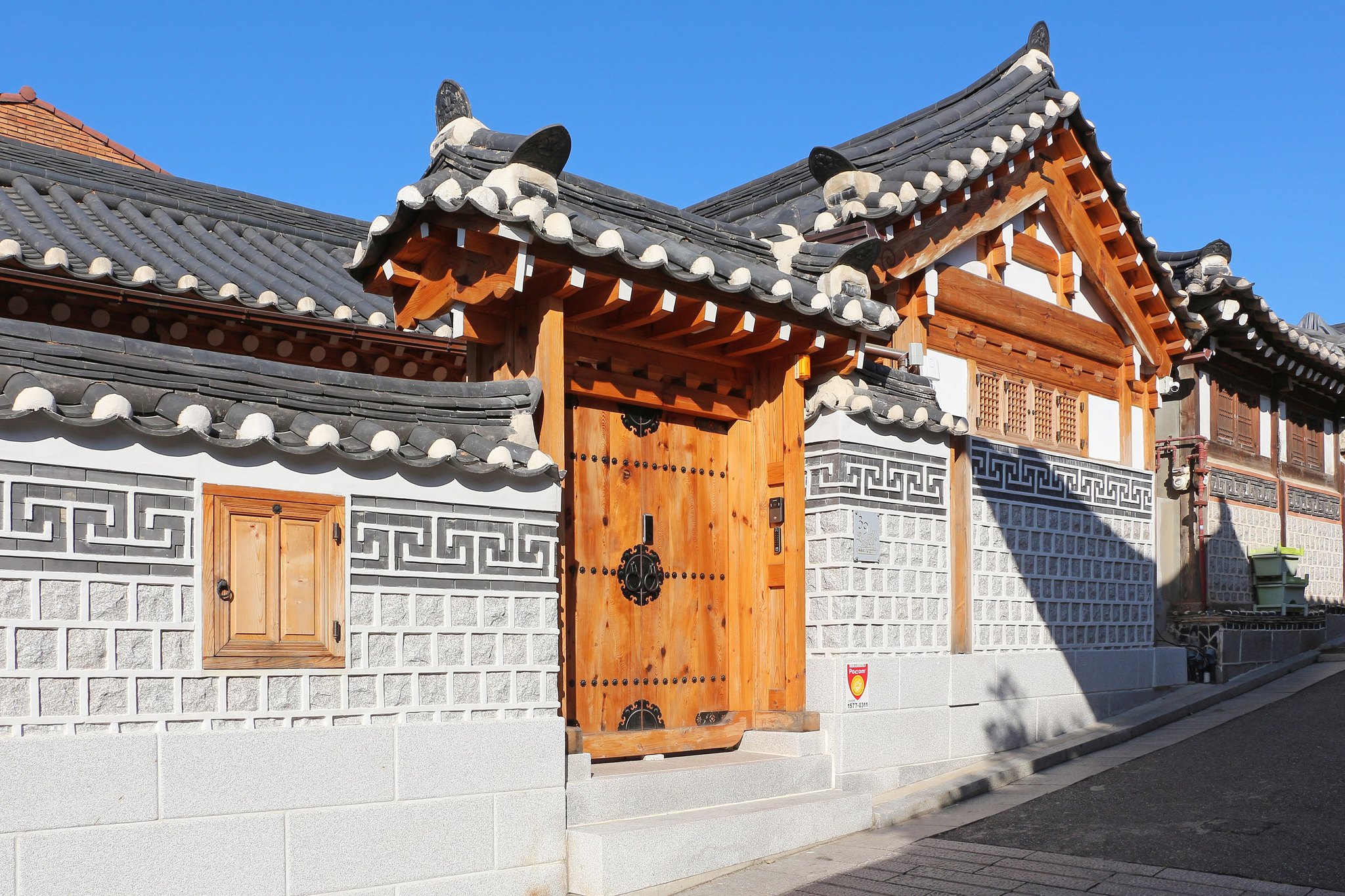 A wooden hanok gate set in a patterned white and grey brick wall in Bukchon
