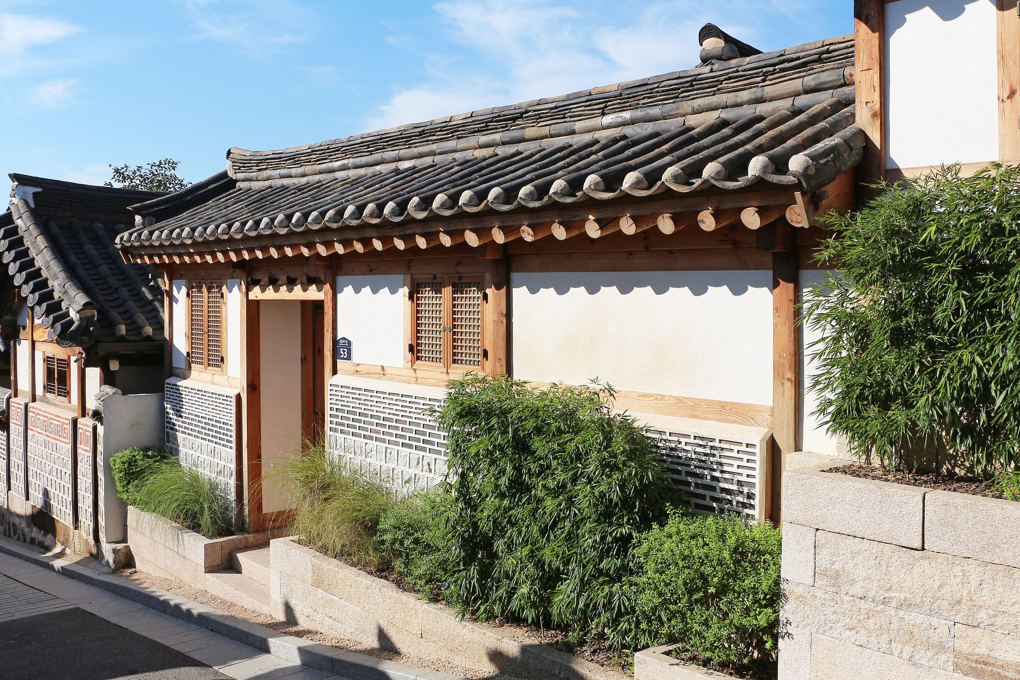 A quiet Bukchon lane between hanok walls with shrubs growing against the stone