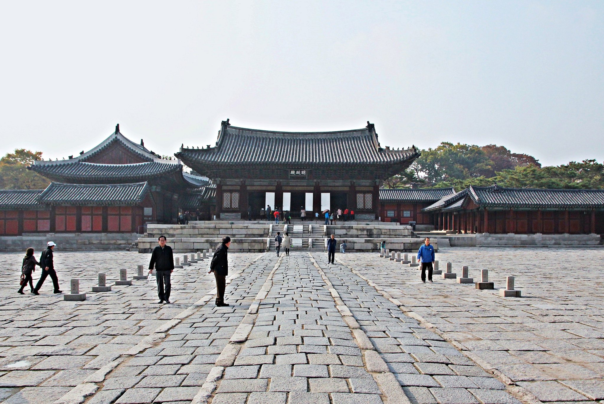 People walking the raised stone path across the courtyard to Myeongjeongjeon in autumn