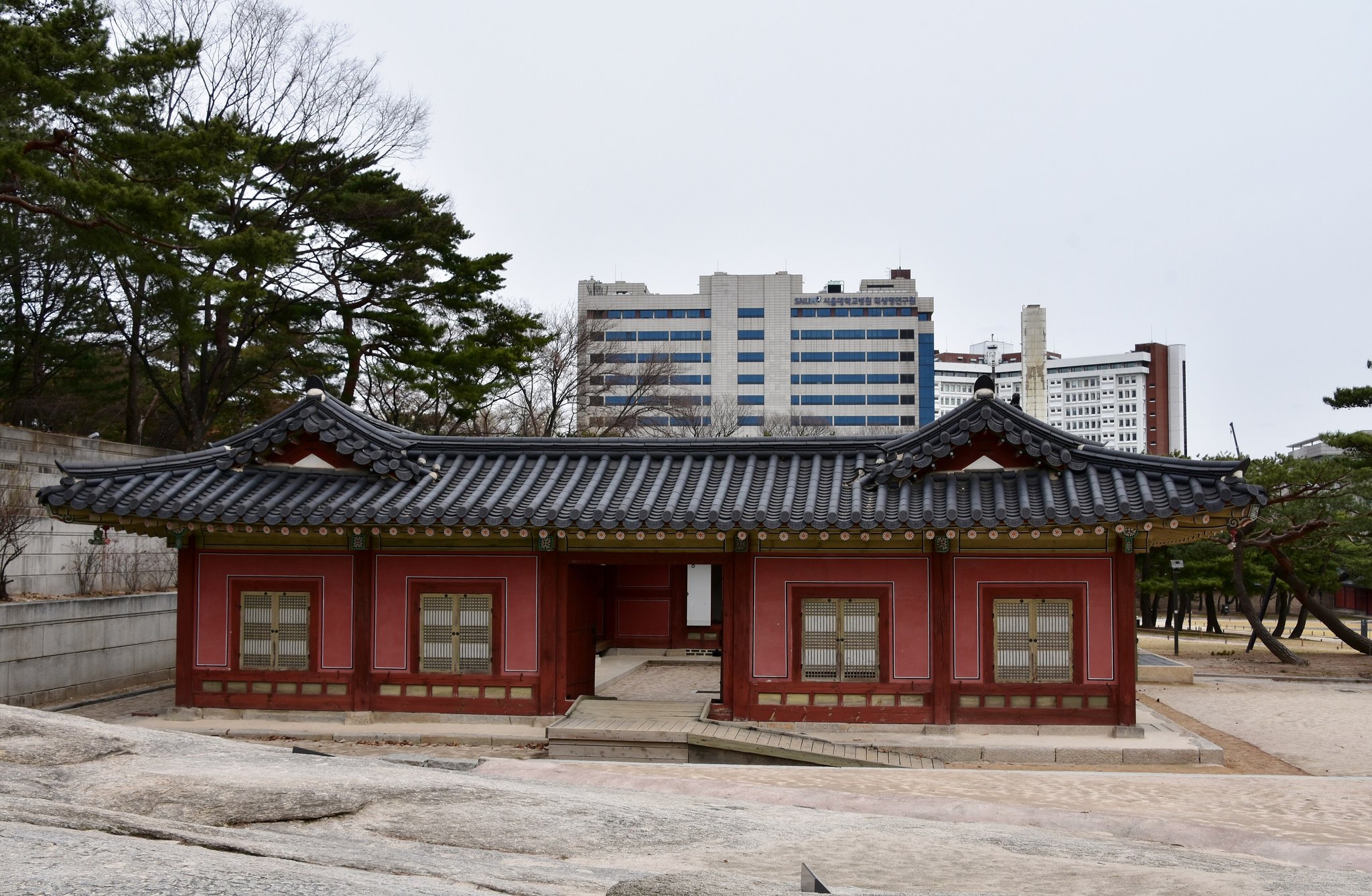 A low red-painted palace building at Changgyeonggung with modern blocks beyond the wall