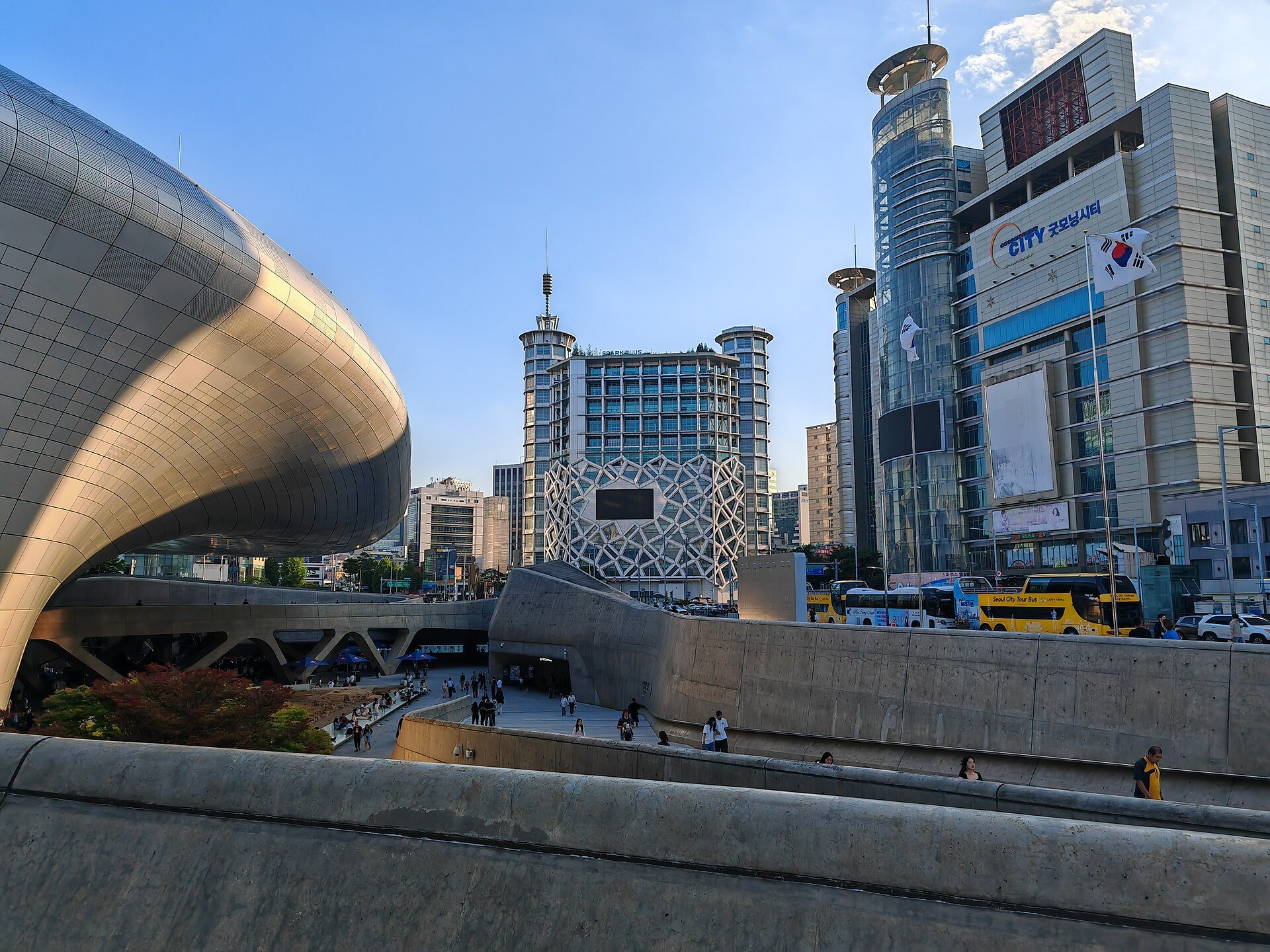 The curved aluminium nose of the Dongdaemun Design Plaza against the surrounding towers