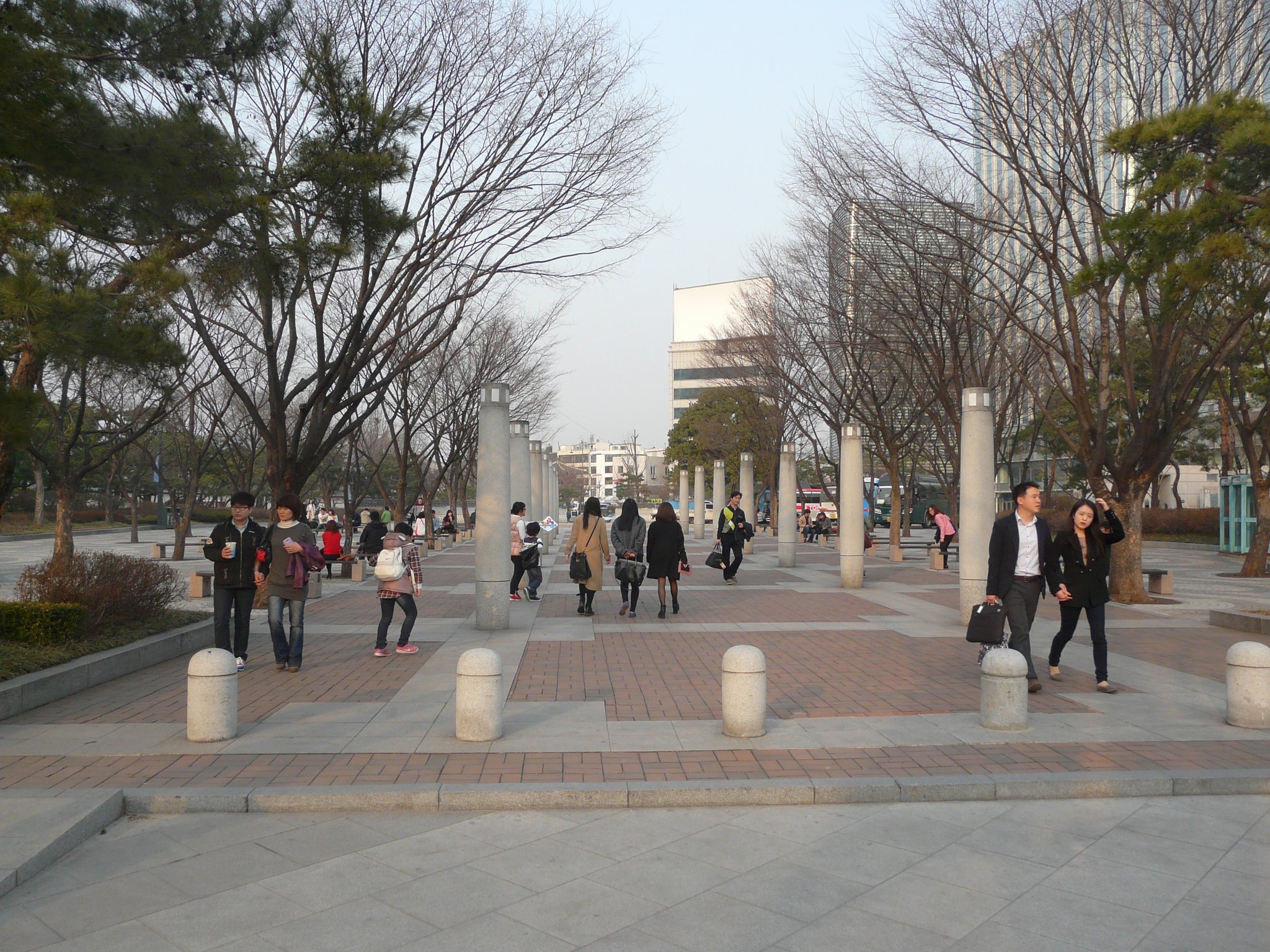 People walking the length of Gwanghwamun Square between bare winter trees