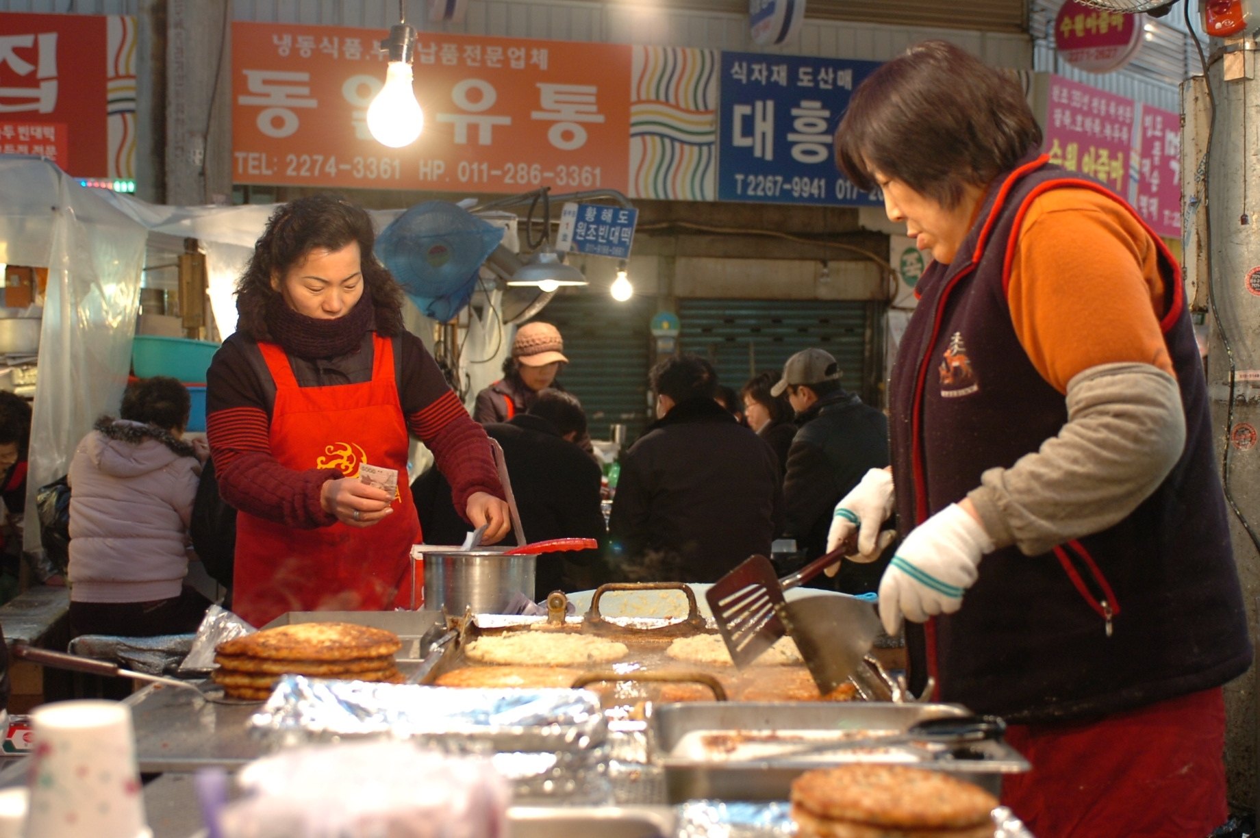 Two women frying bindaetteok mung bean pancakes at a Gwangjang Market stall