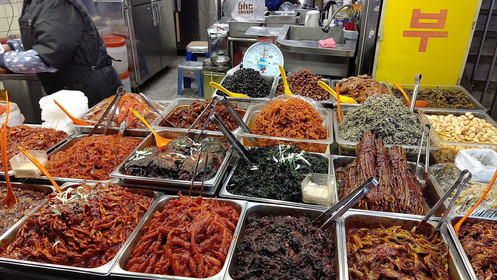 Trays of banchan side dishes in reds and greens at a Gwangjang Market stall