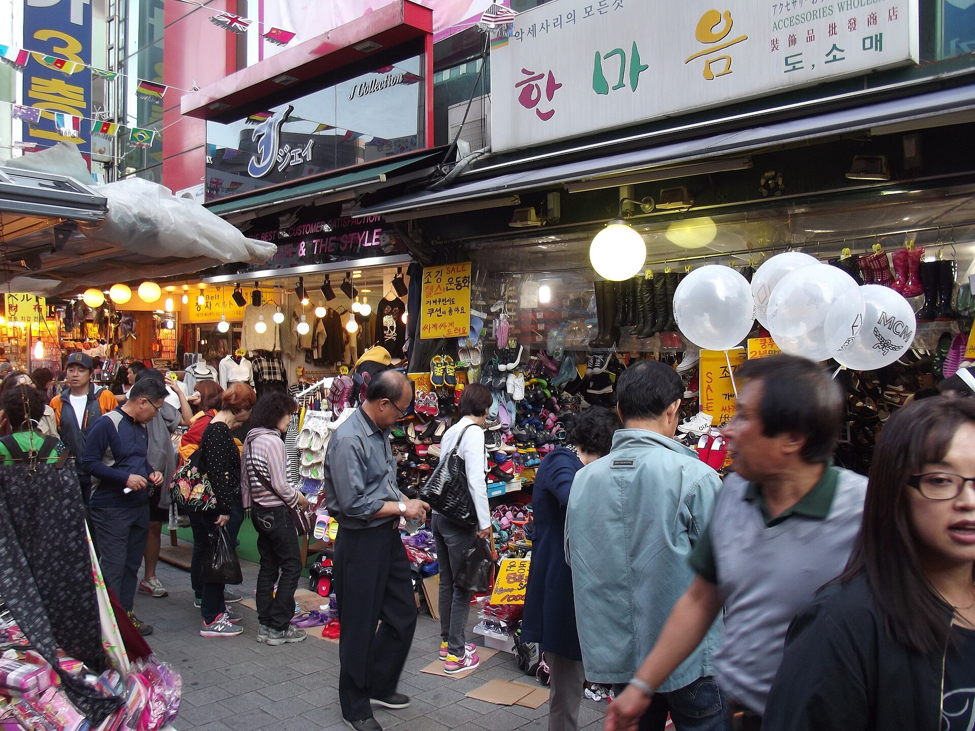A crowded Namdaemun Market alley between stalls hung with goods