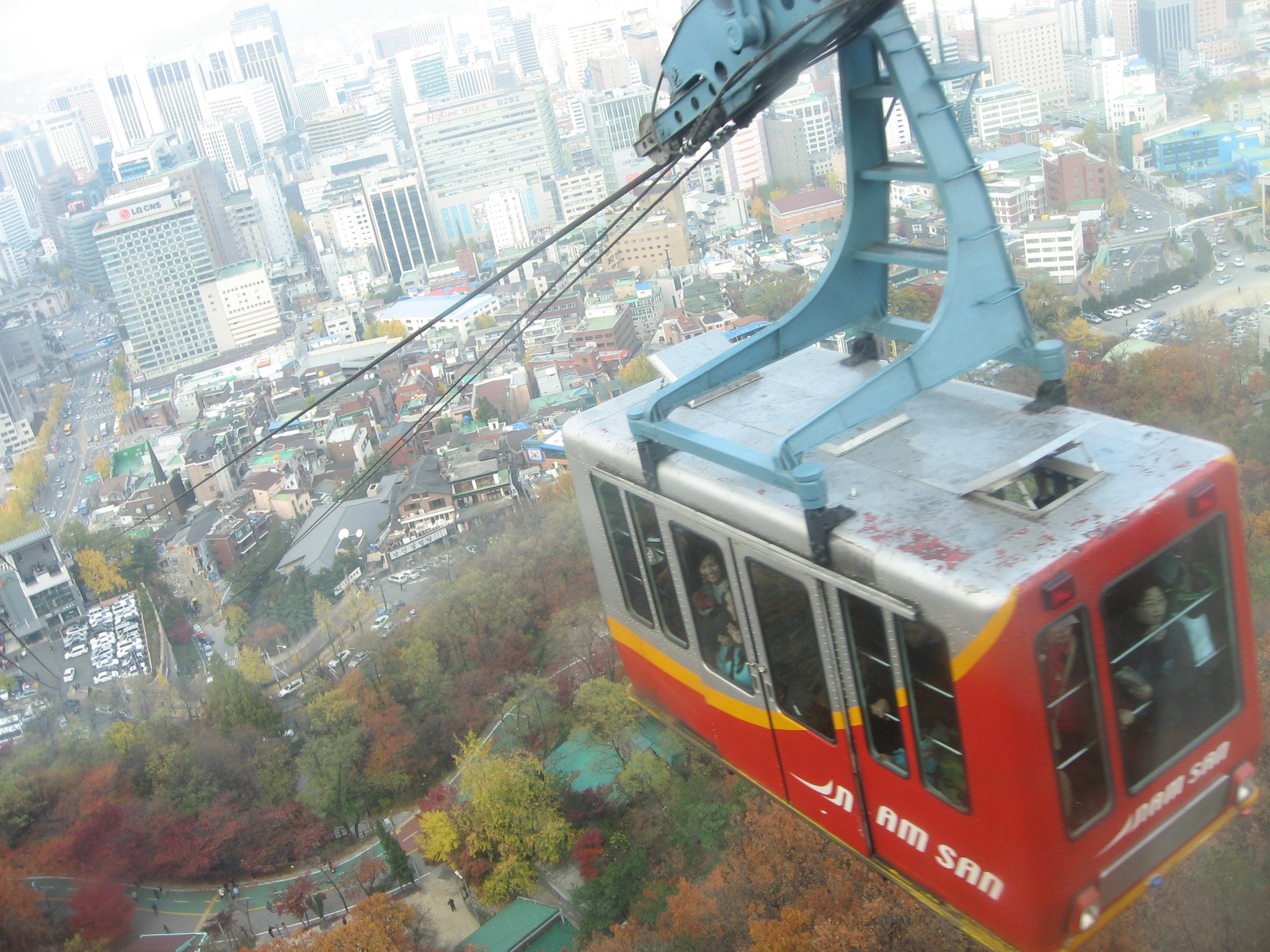 A red Namsan cable car car passing above the autumn trees
